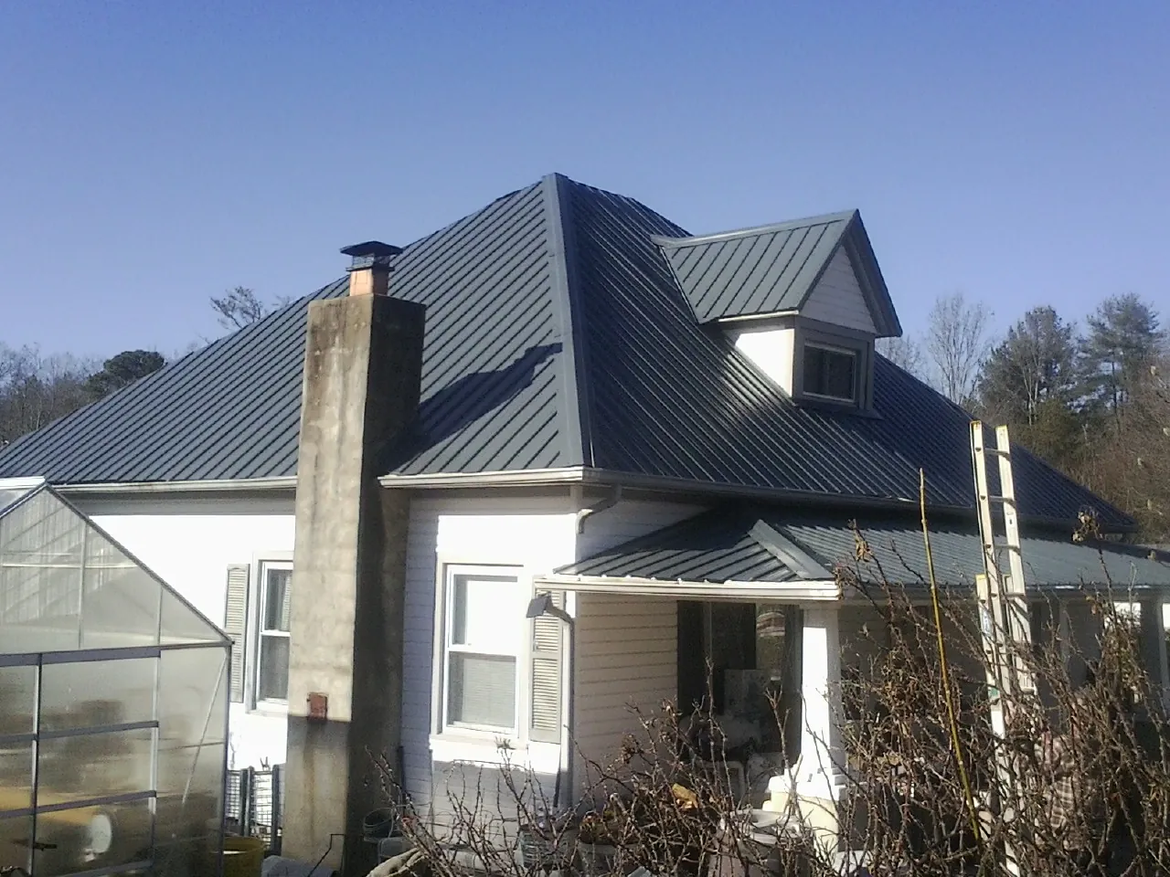 Dark blue standing seam metal roof on a white farmhouse with dormer — Slate & Tile Roof Repair by Roofing Brothers in Nesconset