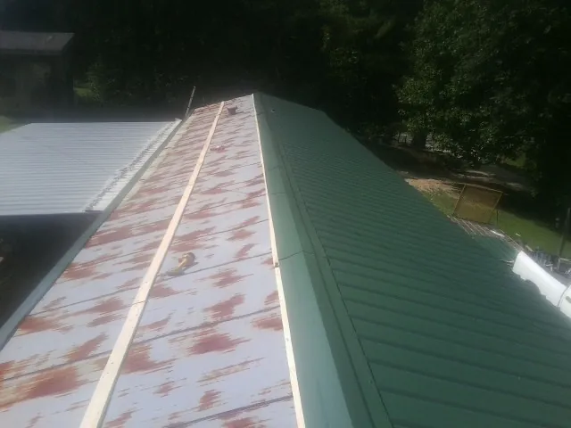 Old rusted panels beside newly installed green metal roofing — Wind Damage Roof Repair by Roofing Brothers in Nesconset