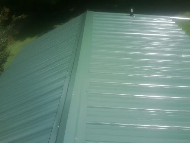 New green metal panels meeting at the ridge of a roof — Flat Roof Repair work by our crew in Nesconset