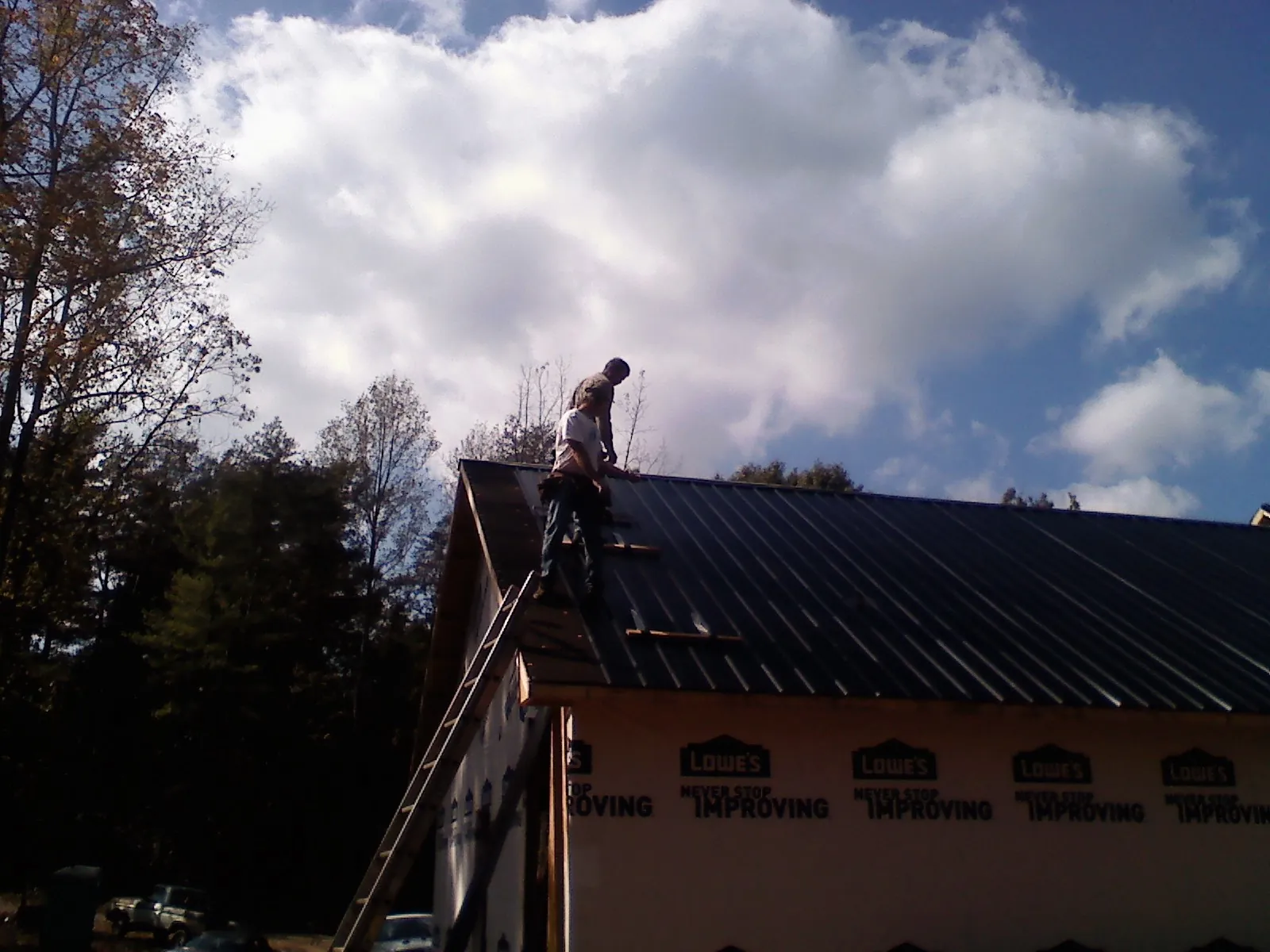Roofer fastening dark metal panels high against a cloudy sky, from a Roof Inspection job in Nesconset