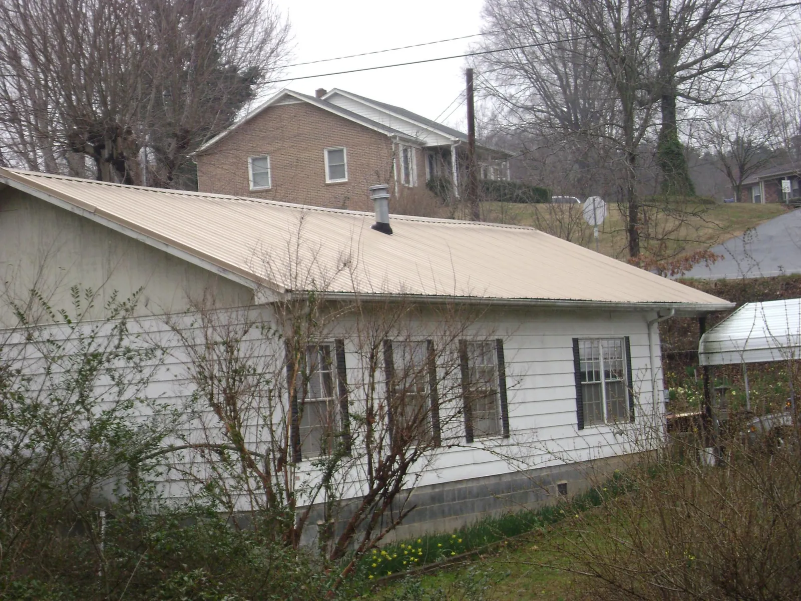 Tan metal roof on a white sided house set into a hillside — Commercial Roofing by Roofing Brothers in Nesconset